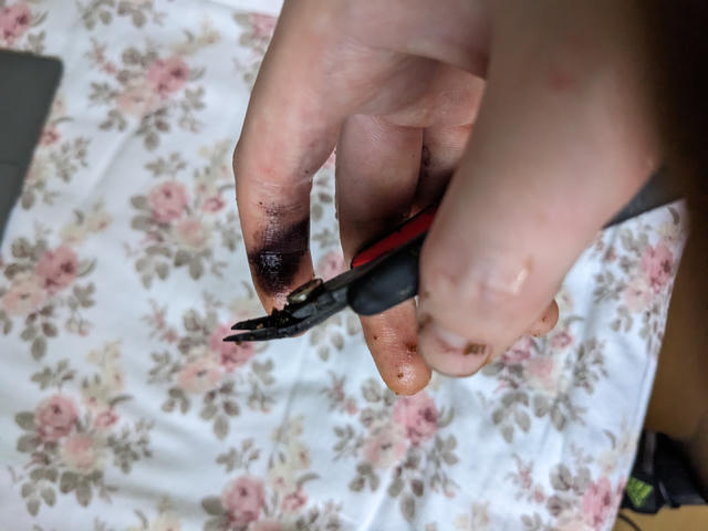 Photo of me holding flush cutters, index finger stained black next to the exposed steel of the cutters.